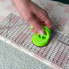 Hand using a green mini clamp on a ruler with a quilt