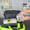 Person packing colorful folded clothes into a black suitcase with a green interior.