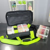 Black travel bag with green straps containing colorful items on a black surface.